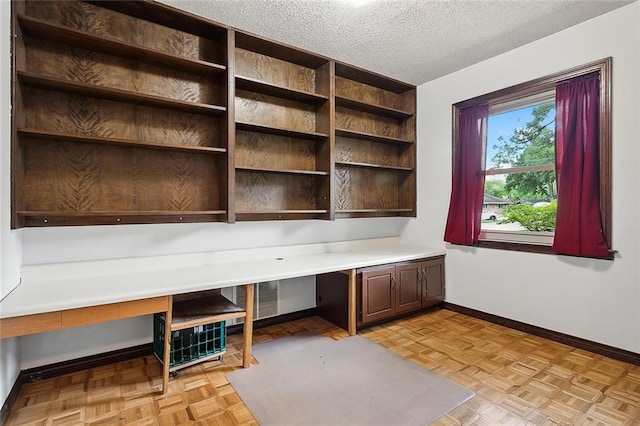 unfurnished office with built in desk, light parquet floors, and a textured ceiling