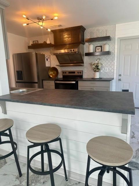 kitchen with ventilation hood, stainless steel appliances, a kitchen bar, and kitchen peninsula