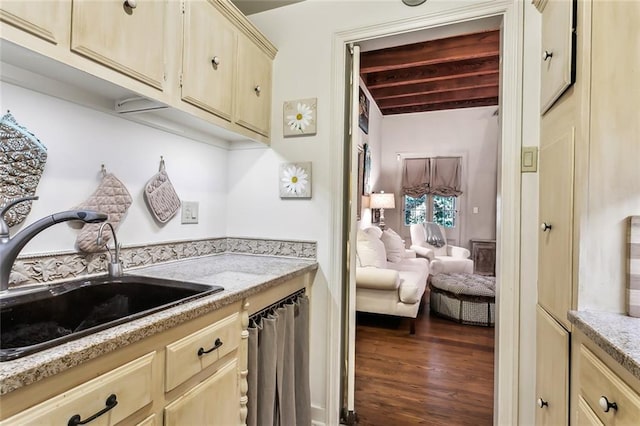 kitchen with dark wood-type flooring, a sink, cream cabinetry, light stone countertops, and beamed ceiling