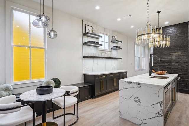 kitchen featuring pendant lighting, open shelves, light wood-style flooring, a kitchen island, and a sink