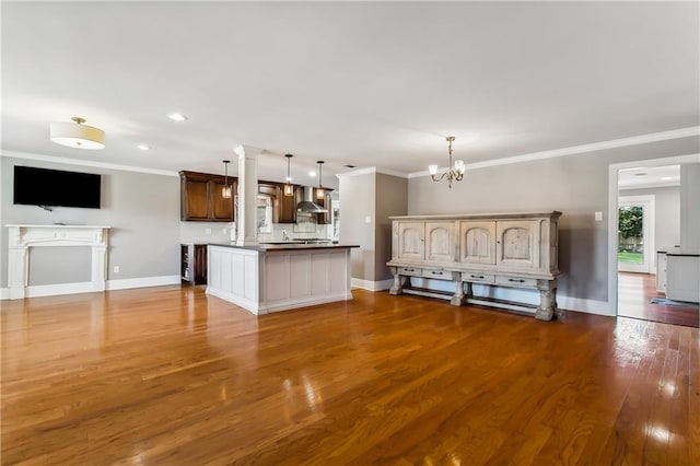 kitchen with wall chimney range hood, decorative light fixtures, crown molding, an inviting chandelier, and dark hardwood / wood-style floors