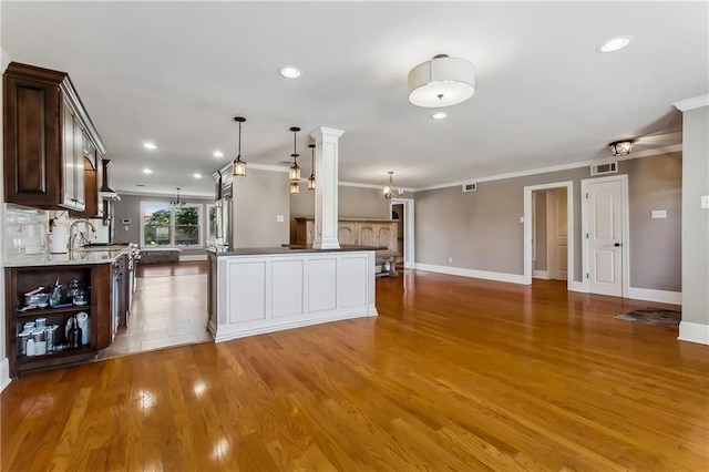 kitchen with hardwood / wood-style flooring, decorative columns, pendant lighting, crown molding, and a center island