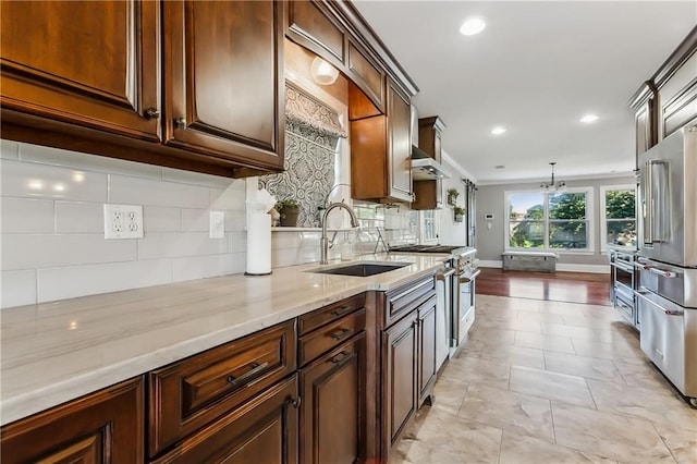 kitchen featuring wall chimney range hood, tasteful backsplash, pendant lighting, high quality appliances, and sink