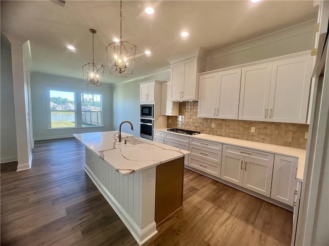 kitchen featuring white cabinetry, decorative light fixtures, a center island with sink, and dark hardwood / wood-style flooring