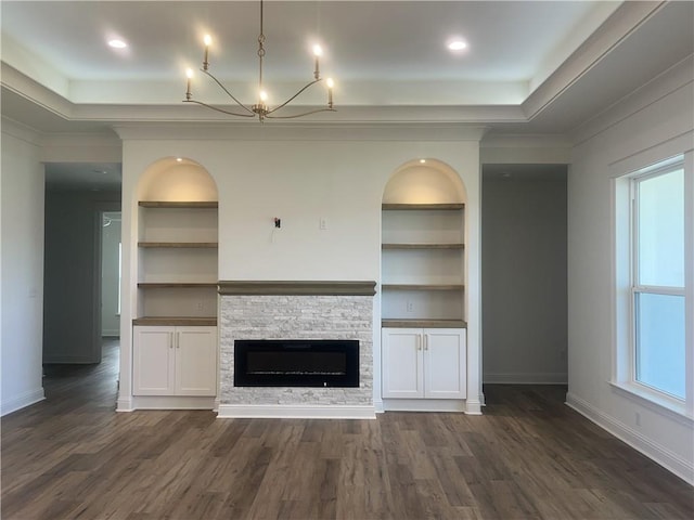 unfurnished living room featuring built in shelves, ornamental molding, a stone fireplace, and dark hardwood / wood-style floors