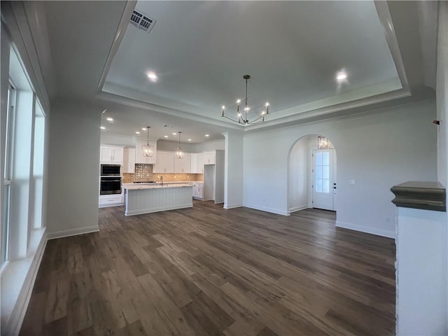 unfurnished living room featuring sink, a notable chandelier, a tray ceiling, and dark hardwood / wood-style floors