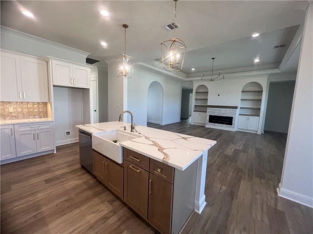 kitchen featuring dishwasher, a kitchen island with sink, a stone fireplace, sink, and white cabinetry