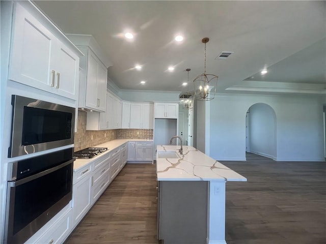 kitchen featuring appliances with stainless steel finishes, an island with sink, white cabinets, light stone counters, and dark hardwood / wood-style floors