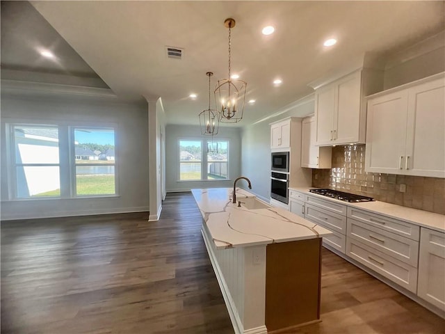 kitchen with white cabinets, a center island with sink, appliances with stainless steel finishes, dark hardwood / wood-style floors, and pendant lighting