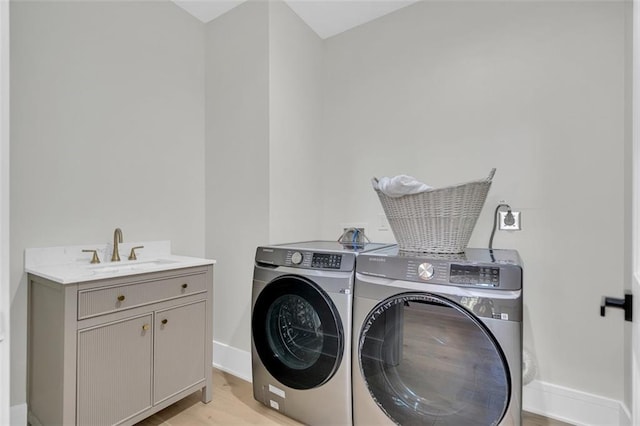 clothes washing area featuring independent washer and dryer, cabinets, sink, and light hardwood / wood-style floors