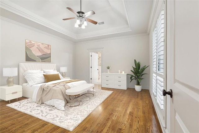 bedroom featuring crown molding, hardwood / wood-style flooring, a raised ceiling, and ceiling fan