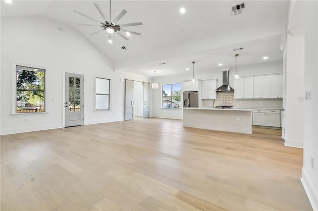 unfurnished living room with light hardwood / wood-style flooring, high vaulted ceiling, a wealth of natural light, and ceiling fan