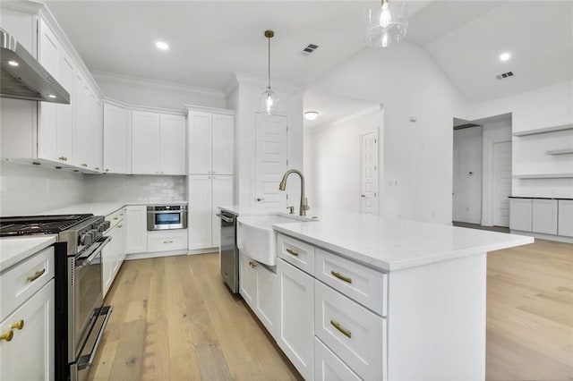 kitchen with wall chimney range hood, sink, stainless steel appliances, white cabinets, and a kitchen island with sink