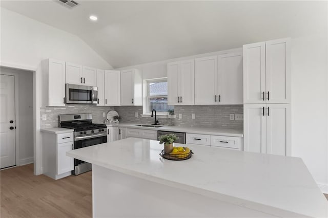 kitchen with lofted ceiling, light hardwood / wood-style flooring, sink, white cabinets, and appliances with stainless steel finishes