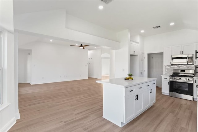 kitchen with appliances with stainless steel finishes, white cabinetry, light wood-type flooring, vaulted ceiling, and a center island