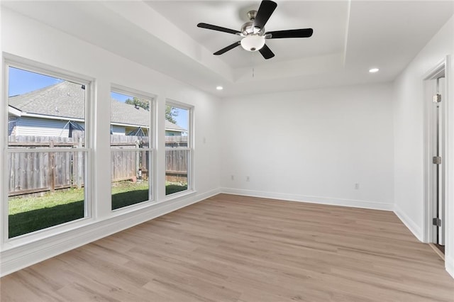 empty room with light hardwood / wood-style floors, a tray ceiling, and ceiling fan