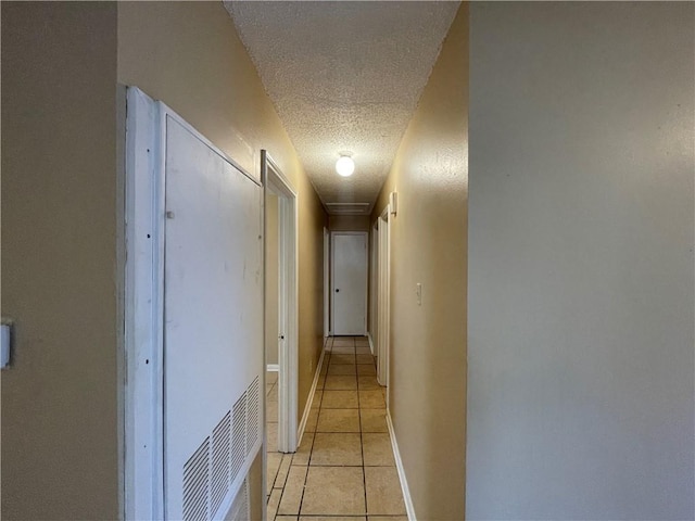 hallway with a textured ceiling and light tile patterned floors