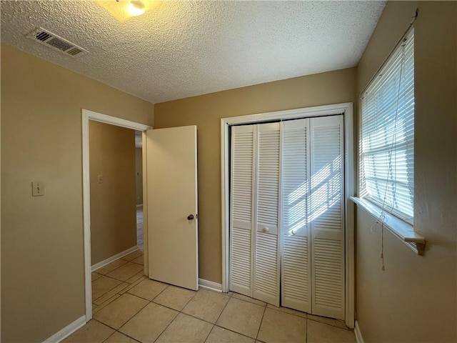 unfurnished bedroom featuring a textured ceiling, a closet, and light tile patterned floors