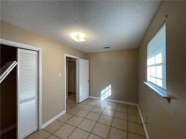 unfurnished bedroom with a closet, a textured ceiling, and light tile patterned flooring