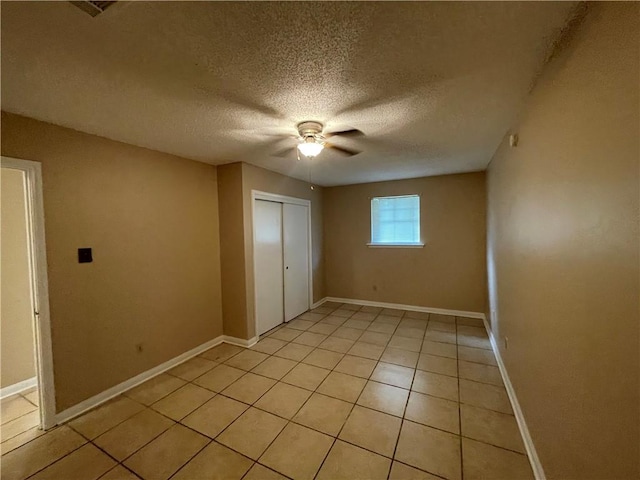 unfurnished bedroom featuring light tile patterned flooring, a textured ceiling, a closet, and ceiling fan