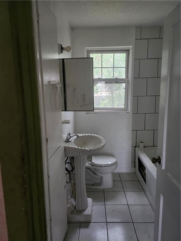 bathroom with toilet, a bathing tub, a textured ceiling, and tile patterned flooring