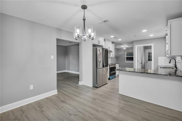 kitchen with tasteful backsplash, appliances with stainless steel finishes, hanging light fixtures, white cabinetry, and light hardwood / wood-style floors