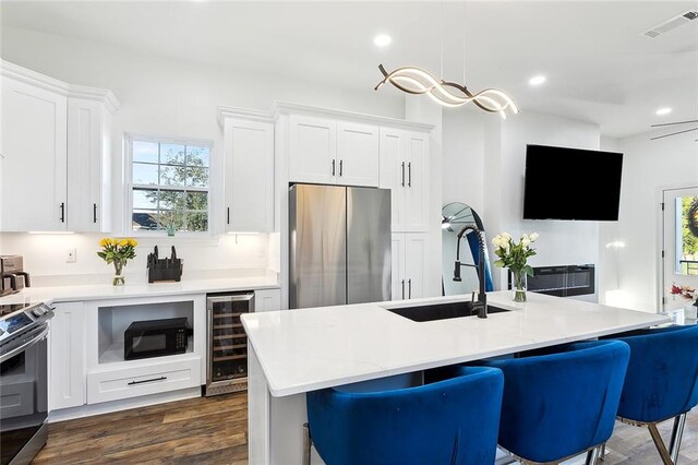 kitchen featuring beverage cooler, an island with sink, stainless steel appliances, white cabinets, and dark hardwood / wood-style floors