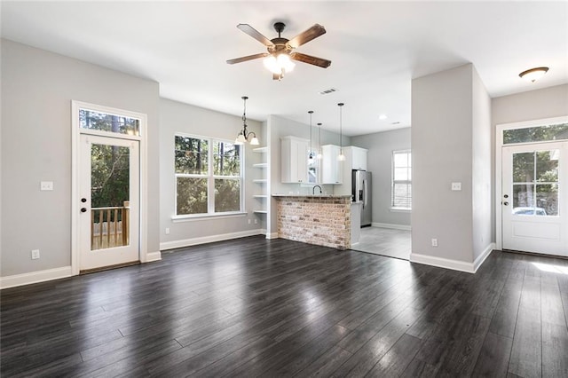 unfurnished living room featuring ceiling fan with notable chandelier and dark hardwood / wood-style flooring