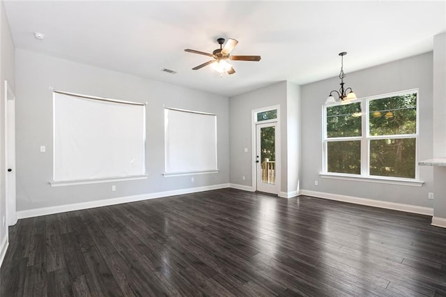 empty room with ceiling fan with notable chandelier, a healthy amount of sunlight, and dark hardwood / wood-style flooring