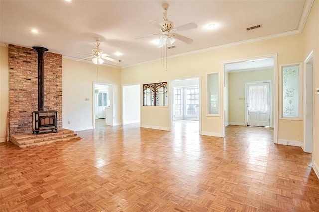 unfurnished living room with a wood stove, light parquet flooring, crown molding, and ceiling fan