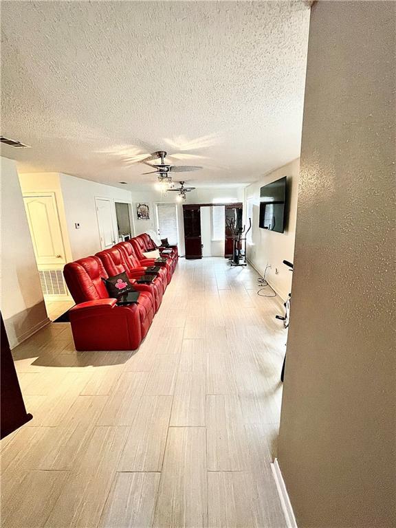 living room featuring ceiling fan, a textured ceiling, and light wood-type flooring