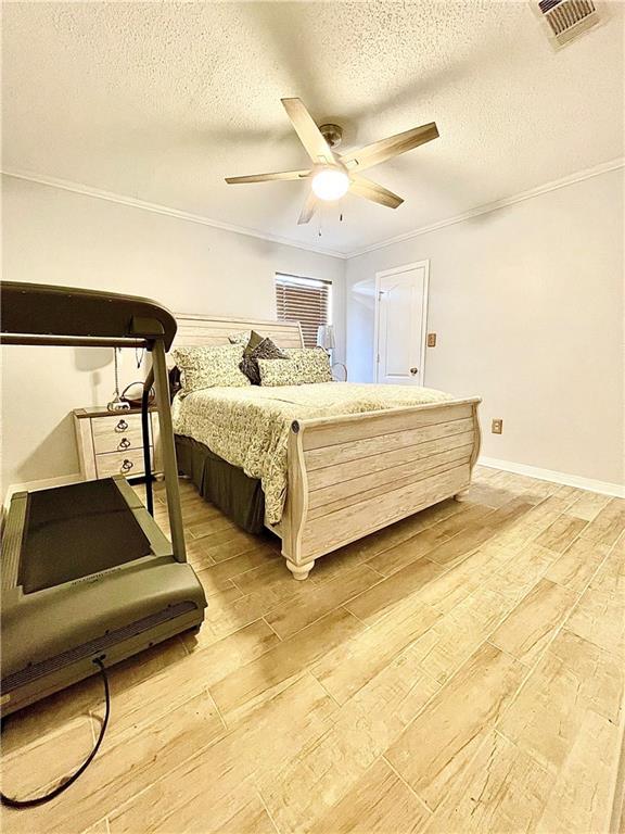 bedroom with ceiling fan, crown molding, a textured ceiling, and light wood-type flooring