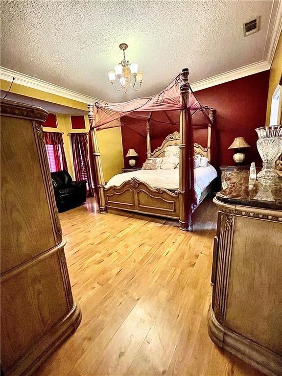 bedroom with a notable chandelier, crown molding, a textured ceiling, and light hardwood / wood-style flooring