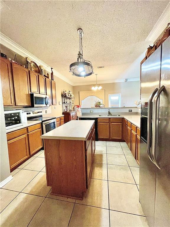 kitchen with light tile patterned floors, appliances with stainless steel finishes, pendant lighting, a kitchen island, and ornamental molding