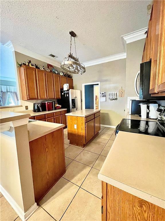 kitchen with appliances with stainless steel finishes, crown molding, pendant lighting, light tile patterned floors, and a center island