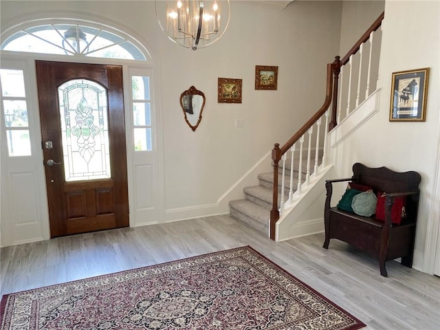 foyer entrance featuring baseboards, a chandelier, wood finished floors, and stairway