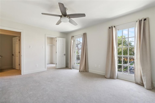 unfurnished bedroom featuring a walk in closet, ceiling fan, access to outside, a closet, and light colored carpet