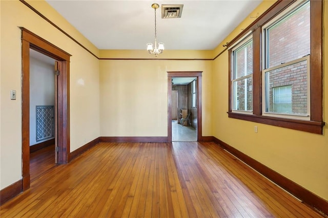 spare room with hardwood / wood-style floors and an inviting chandelier