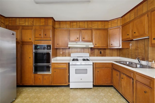 kitchen featuring wood walls, sink, white gas range oven, black double oven, and stainless steel fridge