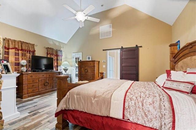 bedroom with high vaulted ceiling, ceiling fan, a barn door, and light hardwood / wood-style floors