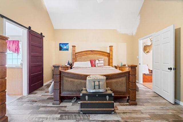 bedroom featuring a barn door, wood-type flooring, and vaulted ceiling