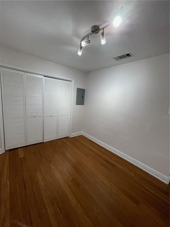 unfurnished bedroom with a closet, electric panel, dark hardwood / wood-style flooring, and track lighting