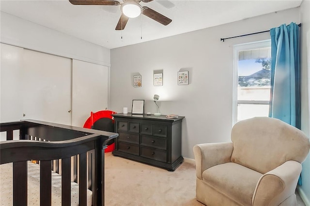 bedroom featuring a nursery area, light colored carpet, and ceiling fan