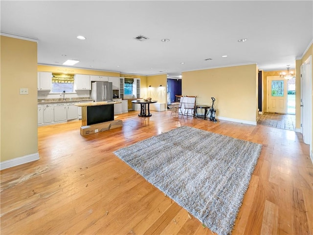 living room with a notable chandelier, sink, ornamental molding, and light hardwood / wood-style floors