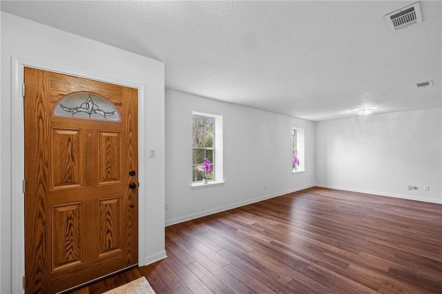 foyer entrance with visible vents, dark wood finished floors, a textured ceiling, and baseboards