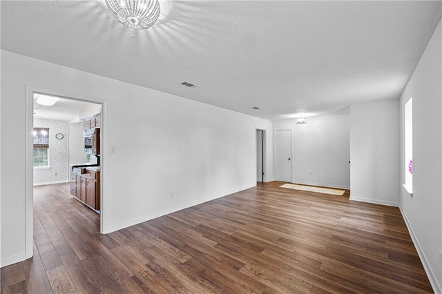 empty room with wallpapered walls, baseboards, visible vents, dark wood finished floors, and a textured ceiling