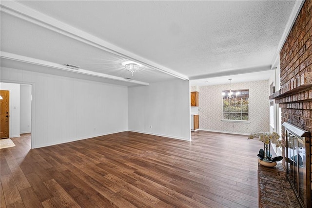 unfurnished living room featuring a textured ceiling, wood finished floors, visible vents, baseboards, and a brick fireplace