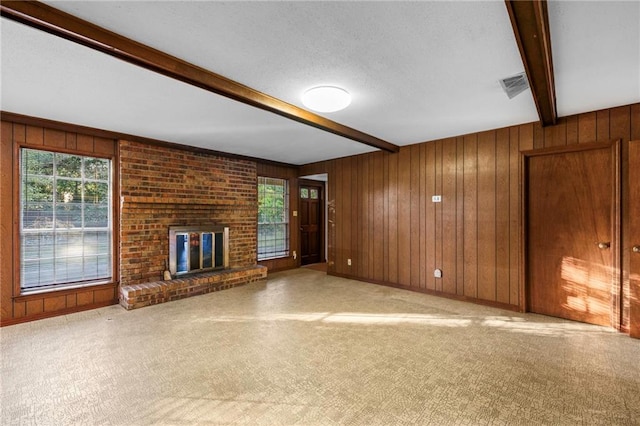 unfurnished living room featuring a textured ceiling, a brick fireplace, wooden walls, beam ceiling, and light colored carpet