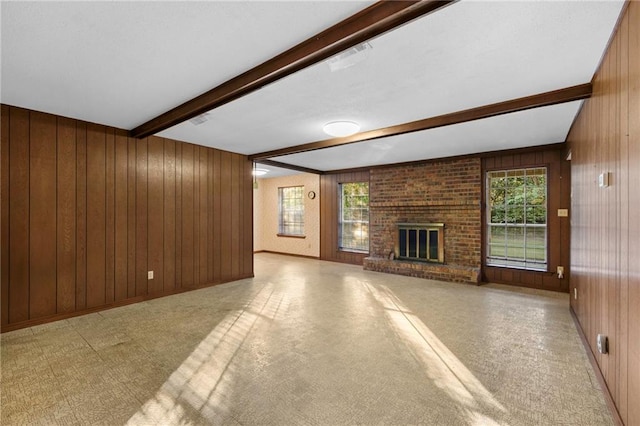 unfurnished living room featuring beamed ceiling, a brick fireplace, a healthy amount of sunlight, and wood walls