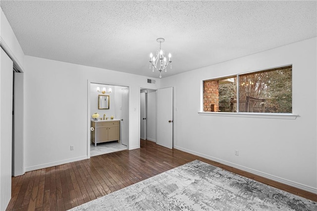 unfurnished bedroom featuring a textured ceiling, wood finished floors, visible vents, and a notable chandelier